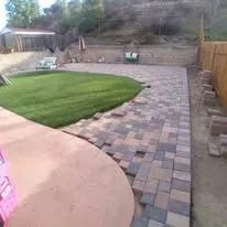 Backyard paver patio with artificial turf and stone accents